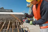 安全装備を身に着けた人が、建設現場でアングルグラインダーを使用して錆びた鉄筋を切断しています。