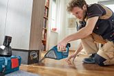 安全装置を装着した人がコードレス掃除機を使用して木くずを掃除しています。