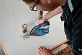 安全装置を装着した人がコードレス掃除機で電気コンセント付近のゴミを掃除しています。