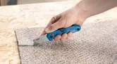 人が折りたたみナイフを使ってカーペットを切ります。