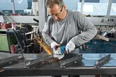 安全装備を身に着けた人がアングルグラインダーで金属の梁を研磨し、火花を発生させます。