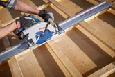 安全装置を装着した人がコードレス丸鋸を使用して木の板を切断しています。.
