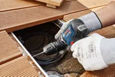 安全装置を装着した人が木製デッキでコードレスドリルドライバーを使用しています。.