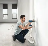 壁のパイプを掘削する男性。