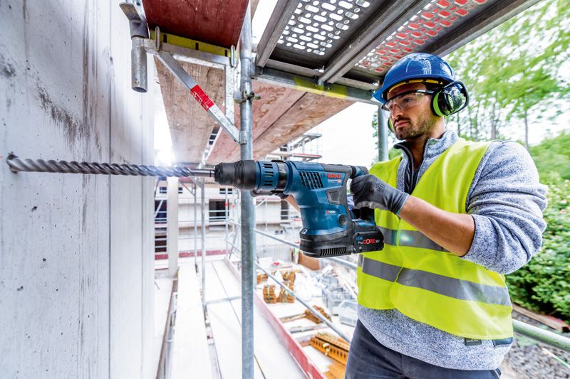 安全装置を装着した人が、コードレス回転ハンマーを使用してコンクリートに穴を開けます。.