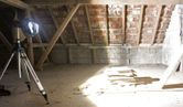 三脚に取り付けられた現場照明が、未完成の屋根裏部屋に積み上げられた板を明るく照らしています。.