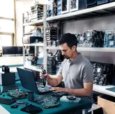 作業台でコードレスドライバーを使用して電子部品を組み立てている人。