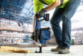 安全装備を身に着けた人が、集塵装置が組み込まれた工具でコンクリートを掘削しています。
