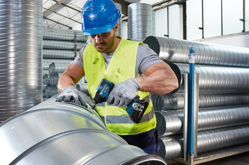 安全装置を装着した人が、コードレス電動工具を使用して金属ダクトを固定しています。.