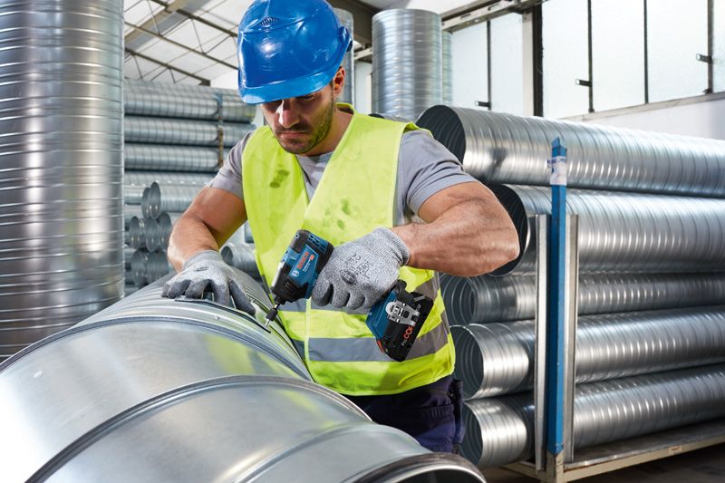 安全装置を装着した人が、コードレス電動工具を使用して金属ダクトを固定しています。.