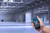 大きな空の工業倉庫で、ある人がレーザー測定器を使用しています。