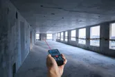 未完成のコンクリートの部屋でレーザー測定器を使って距離を測定する人。.