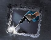 安全装備を身に着けた人が解体用ハンマーを使ってコンクリートの壁を壊しています。