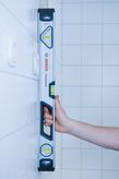 タイル張りの壁に対して 60cm の光学水準器を垂直に立てている人。