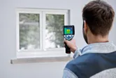 サーモカメラを使用して建物の外から窓を検査している人。