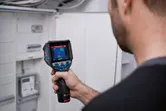 人がサーモカメラを使用して電気パネルを検査しています。