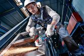 安全装備を身に着けた人が電動工具で金属の梁を研磨し、火花を発生させます。