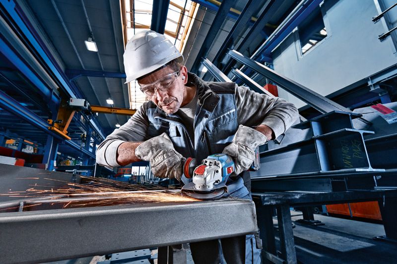 安全装置を装着した人がコードレスアングルグラインダーで金属を研磨し、火花を発生させます。