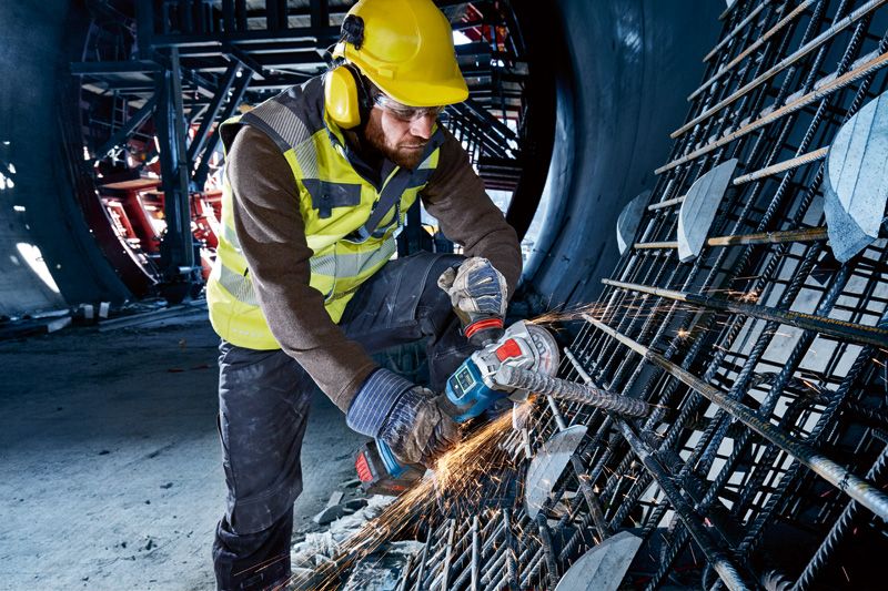 安全装置を装着した人がコードレスアングルグラインダーを使用して金属鉄筋を切断しています。