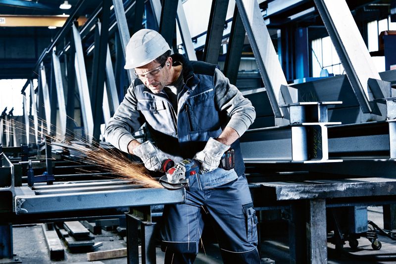 安全装置を装着した人がコードレスアングルグラインダーで金属の梁を研磨しています。.