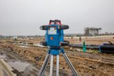濡れた建設現場に三脚に取り付けられたレーザーレベル測定ツールが立っています。