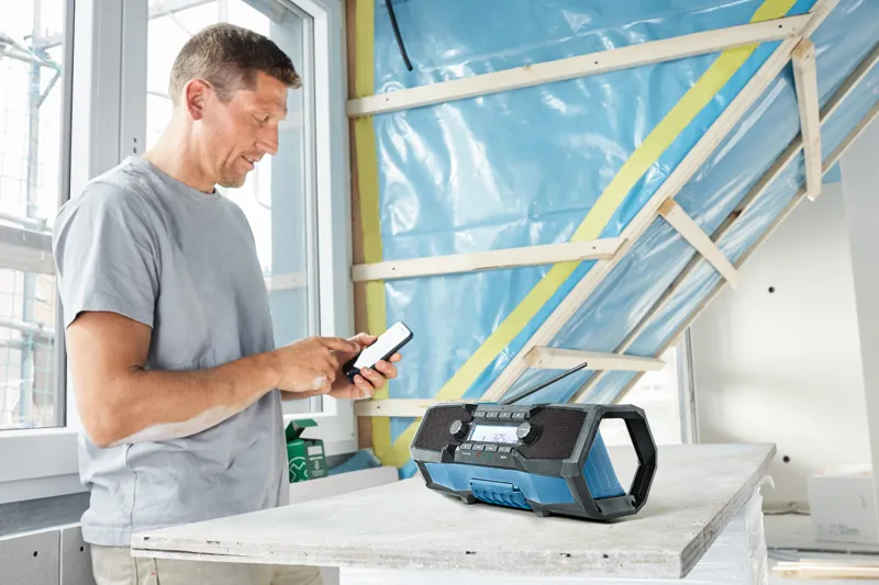 作業服を着た人が、テーブルの上の現場用無線機の横でスマートフォンを調整しています。.