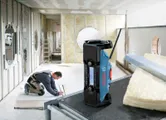 人が建設現場で乾式壁パネルを設置しており、テーブルの上には携帯ラジオが置かれている。