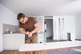安全装置を装着した人が、モダンなキッチンのホワイトボードにドリルで穴を開けています。.