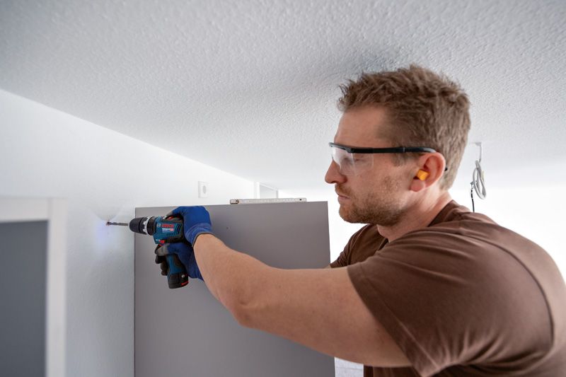 安全装置を装着した人が家具を設置しながら壁に穴を開けています。.