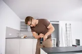 安全装置を装着した人がキッチンキャビネット上でコードレスコンビドリルを使用しています。.