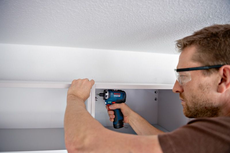 安全装置を装着した人がコードレスドライバーを使用してキャビネットを組み立てています。.