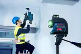 安全装置を装着した人が、レーザーレベルツールのガイドに従って天井に穴を開けます。