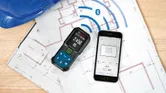 建築図面上の測定値を表示するレーザー測定器とスマートフォン。