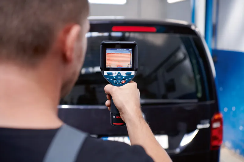 人がサーモカメラを使用して車両の後部窓をスキャンしています。.