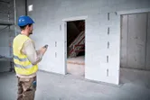 安全装置を装着した人が、建設現場でレーザー測定器を使用して出入口の寸法をチェックしています。