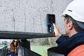 安全装備を身に着けた人が電子検出器でコンクリート梁をスキャンします。
