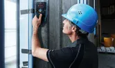 安全装備を身に着けた人が探知機でコンクリートの壁をスキャンします。