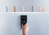 人が探知機を使って壁をスキャンし、隠された物体を探し出す。