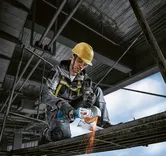 安全装備を身に着けた人が建設現場で金属を研磨し、火花を散らしている。