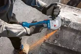 安全装備を身に着けた人がアングルグラインダーでコンクリートを研磨し、火花を散らしています。