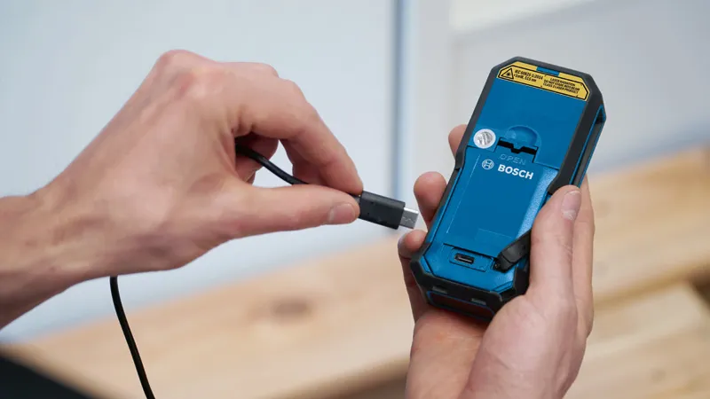 手持ち式電動工具の背面に充電ケーブルを接続している人。.