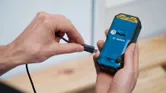 手持ち式電動工具の背面に充電ケーブルを接続している人。