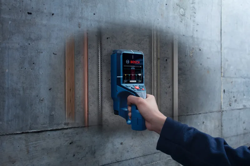 人が電子探知機を使ってコンクリートの壁をスキャンし、隠されたパイプや電線の位​​置を特定する。