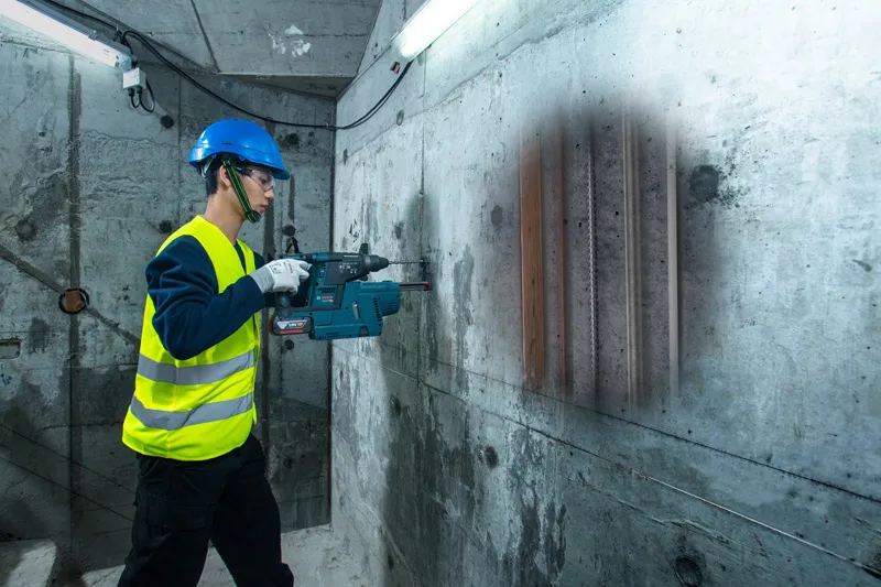 安全装備を身に着けた人が探知機でコンクリートの壁をスキャンし、内部のパイプを明らかにします。.