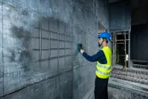 安全装備を身に着けた人が検出器でコンクリートの壁をスキャンし、鉄筋の位置を特定します。