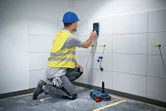 安全装備を身に着けた人がタイル張りの壁で壁スキャナーを使用しています。