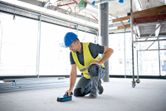 安全装備を身に着けた人が壁スキャナーで建設現場の床をスキャンします。.