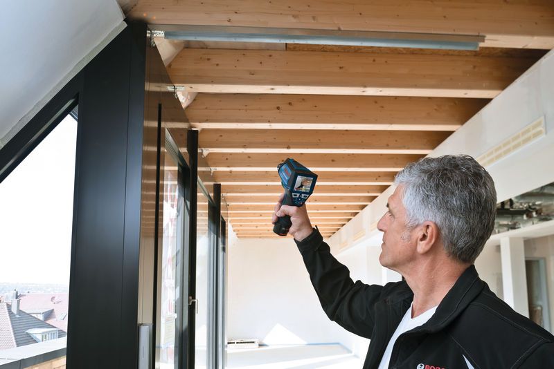 人が手持ち式の検査装置を使って天井の梁をスキャンしています。