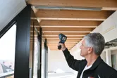 明るい部屋の中で、人が温度検出器を使って木製の天井をスキャンしています。