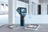 未完成の部屋にある 2 つのタブレットの横のテーブルの上に、デジタル ディスプレイ付きの温度検出器が置かれています。